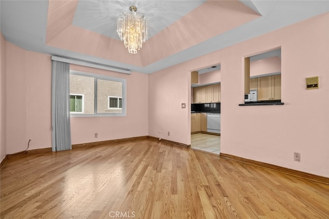 empty room featuring a chandelier, light hardwood / wood-style floors, and a tray ceiling