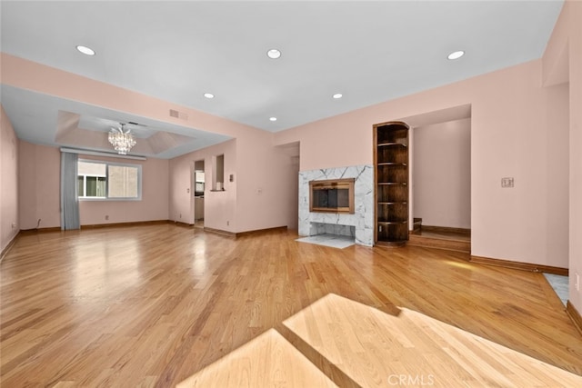 unfurnished living room with light hardwood / wood-style flooring, a chandelier, a premium fireplace, and a tray ceiling