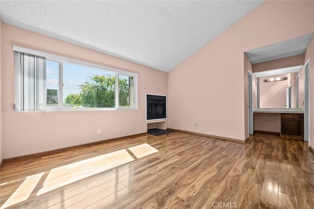 unfurnished living room featuring a textured ceiling, vaulted ceiling, and hardwood / wood-style floors