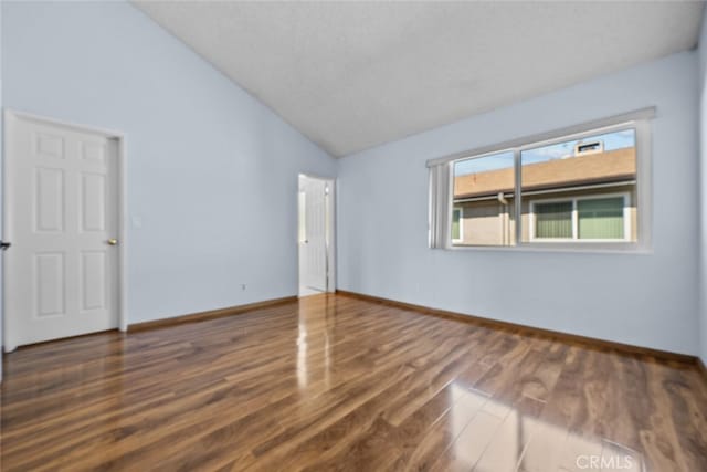 spare room featuring a textured ceiling, dark wood-type flooring, and vaulted ceiling