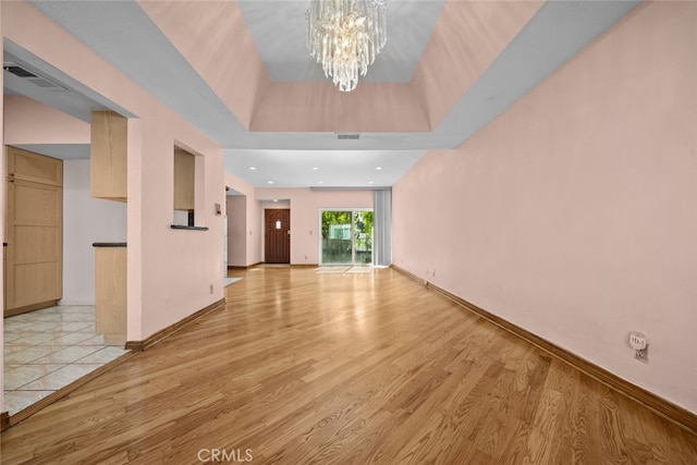 interior space featuring a raised ceiling, a chandelier, and light hardwood / wood-style floors