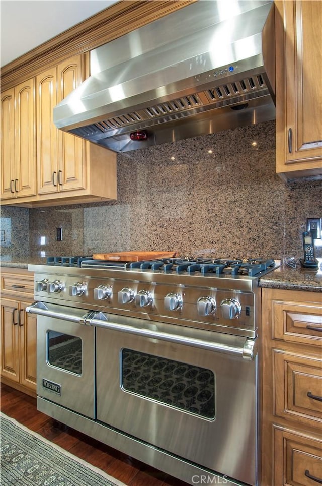 kitchen with tasteful backsplash, dark hardwood / wood-style flooring, dark stone counters, range hood, and range with two ovens