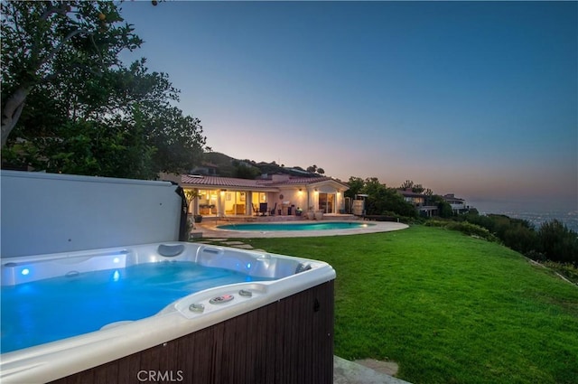 pool at dusk featuring a yard and a hot tub