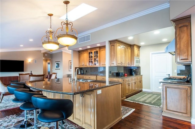 kitchen featuring ornamental molding, a kitchen island with sink, dark hardwood / wood-style flooring, and decorative light fixtures