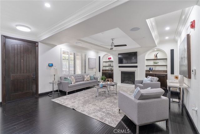 living room featuring built in shelves, ornamental molding, dark hardwood / wood-style floors, and ceiling fan