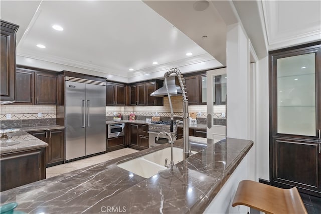 kitchen with dark stone counters, dark brown cabinets, decorative backsplash, and built in appliances