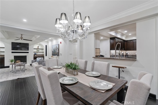 dining space with ceiling fan with notable chandelier, a tray ceiling, built in features, ornamental molding, and dark hardwood / wood-style floors