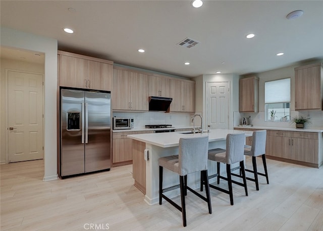 kitchen featuring light brown cabinets, a center island with sink, appliances with stainless steel finishes, light wood-type flooring, and sink