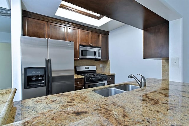 kitchen with backsplash, light stone countertops, sink, and appliances with stainless steel finishes