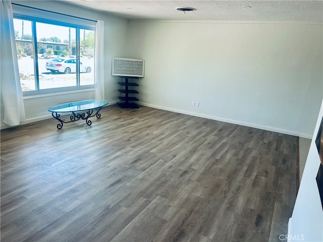 empty room with a textured ceiling, crown molding, and dark hardwood / wood-style flooring