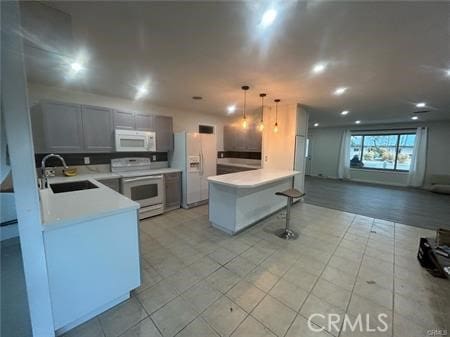 kitchen with pendant lighting, sink, white appliances, gray cabinets, and a kitchen breakfast bar