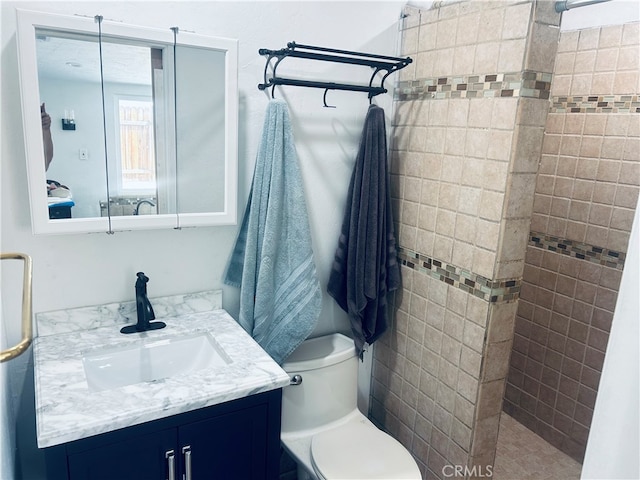 bathroom featuring a tile shower, vanity, and toilet