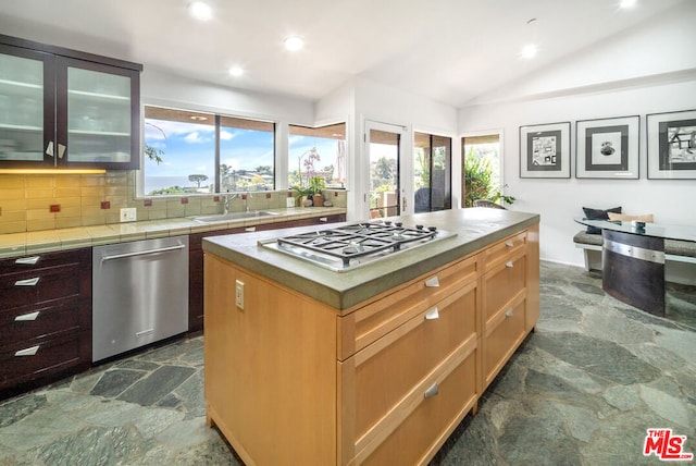 kitchen featuring lofted ceiling, decorative backsplash, a kitchen island, sink, and stainless steel appliances