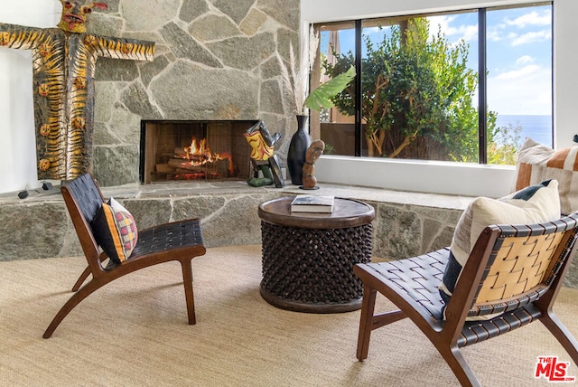 sitting room featuring a wealth of natural light, carpet, a stone fireplace, and a water view