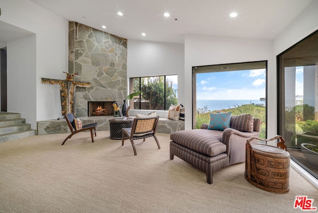 carpeted living room featuring a water view, high vaulted ceiling, a healthy amount of sunlight, and a stone fireplace