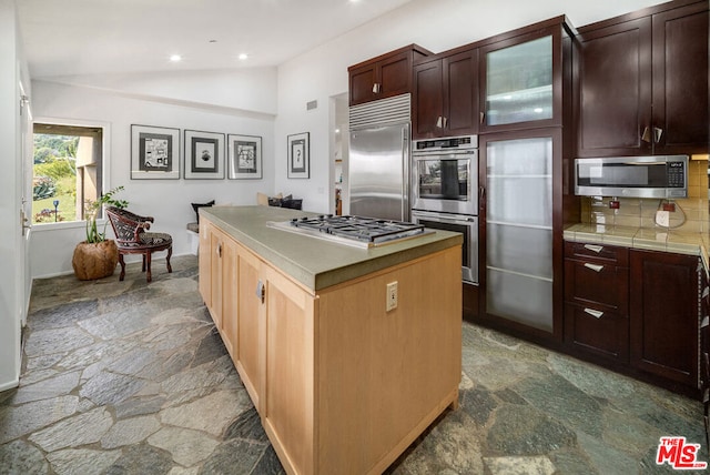 kitchen with backsplash, stainless steel appliances, lofted ceiling, and a kitchen island