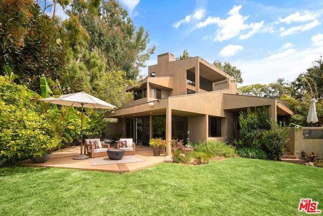 back of property featuring a balcony, an outdoor living space, and a lawn