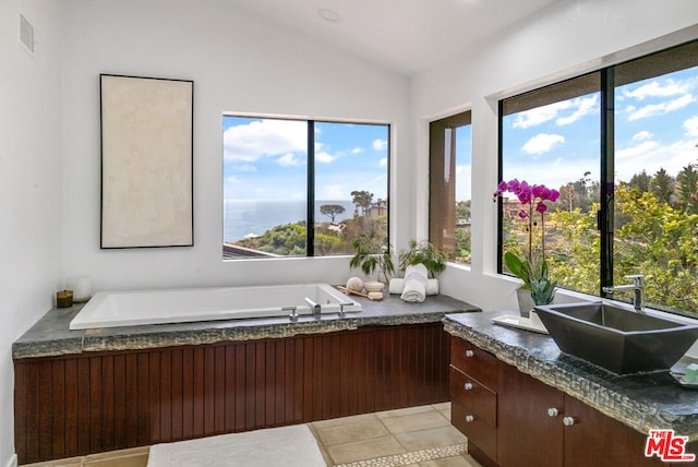 miscellaneous room featuring a tub to relax in, vanity, vaulted ceiling, a water view, and tile patterned flooring