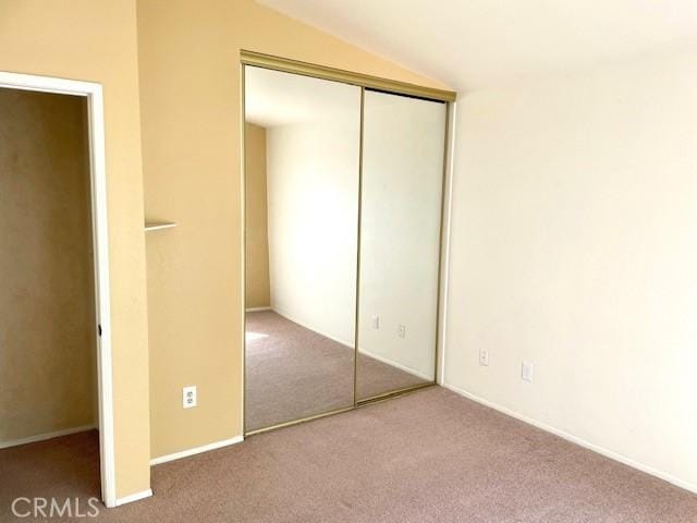 unfurnished bedroom featuring carpet, a closet, and vaulted ceiling