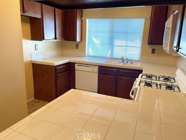 kitchen with tile countertops, plenty of natural light, white appliances, and sink