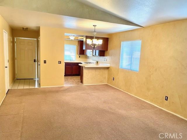 kitchen with a notable chandelier, light colored carpet, kitchen peninsula, and hanging light fixtures