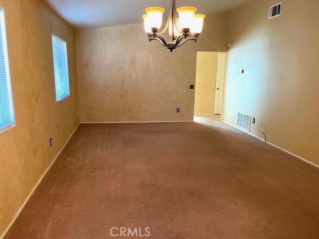 empty room with carpet flooring and an inviting chandelier