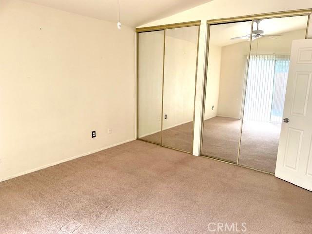 unfurnished bedroom with carpet flooring, two closets, and lofted ceiling