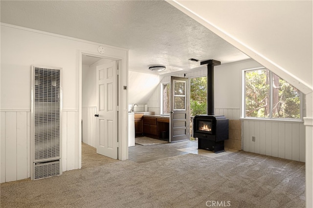 unfurnished living room featuring wood walls, a wood stove, a textured ceiling, light carpet, and vaulted ceiling