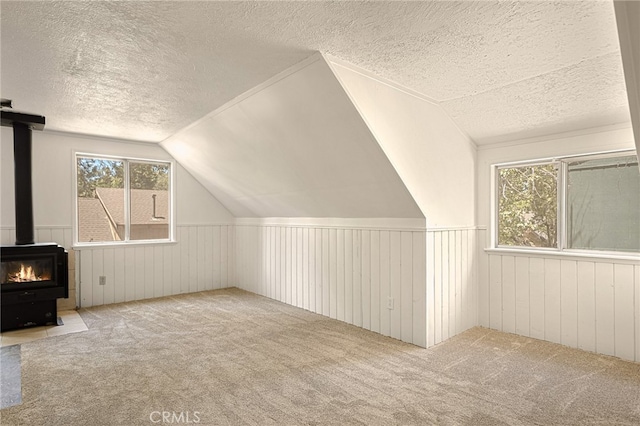 bonus room with light colored carpet, a textured ceiling, and a wood stove