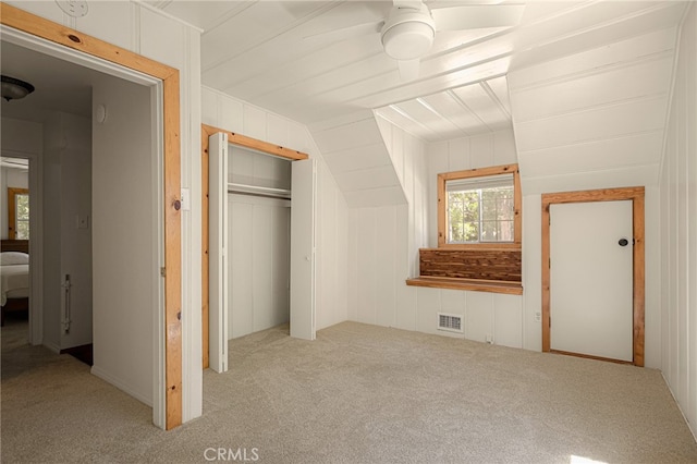 unfurnished bedroom with ceiling fan, light colored carpet, wooden walls, and a closet