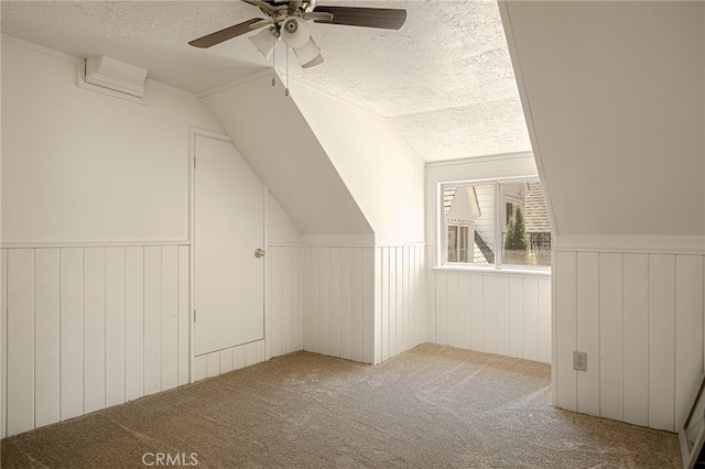 bonus room featuring ceiling fan, wood walls, a textured ceiling, carpet floors, and vaulted ceiling