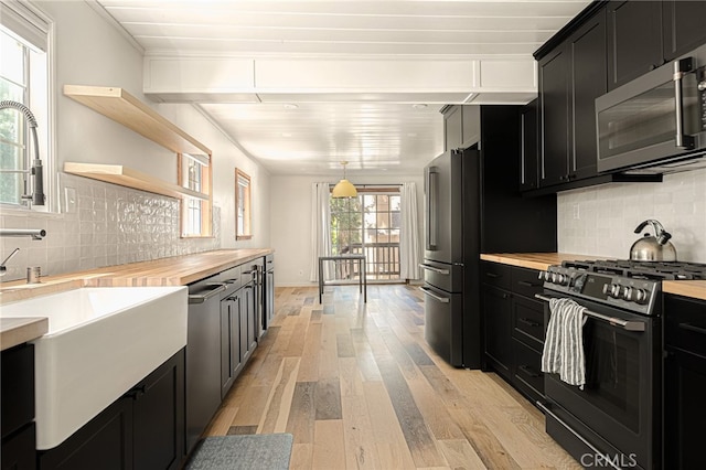 kitchen with decorative backsplash, light wood-type flooring, appliances with stainless steel finishes, and wooden counters