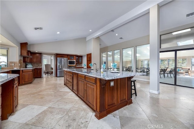 kitchen featuring light stone countertops, a center island with sink, stainless steel appliances, and a healthy amount of sunlight