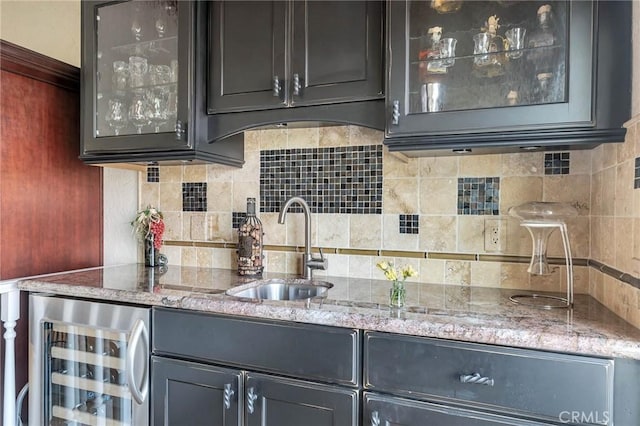 kitchen with backsplash, light stone counters, sink, and beverage cooler