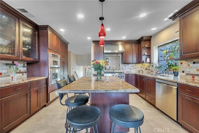 kitchen with wall chimney exhaust hood, decorative backsplash, appliances with stainless steel finishes, decorative light fixtures, and a breakfast bar area