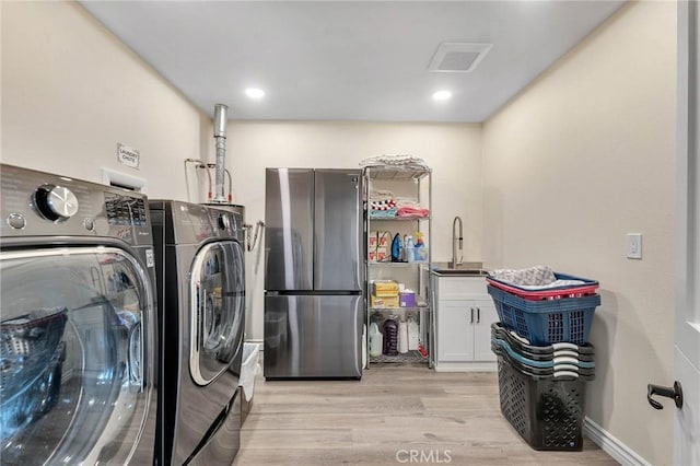 washroom featuring washing machine and dryer, cabinets, sink, and light hardwood / wood-style floors