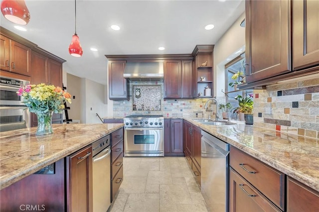 kitchen with pendant lighting, wall chimney range hood, sink, light stone countertops, and stainless steel appliances