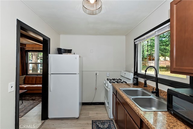 kitchen featuring sink, stainless steel gas stove, light hardwood / wood-style flooring, light stone countertops, and white fridge