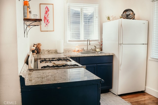 kitchen featuring light wood-type flooring, white appliances, sink, and blue cabinetry