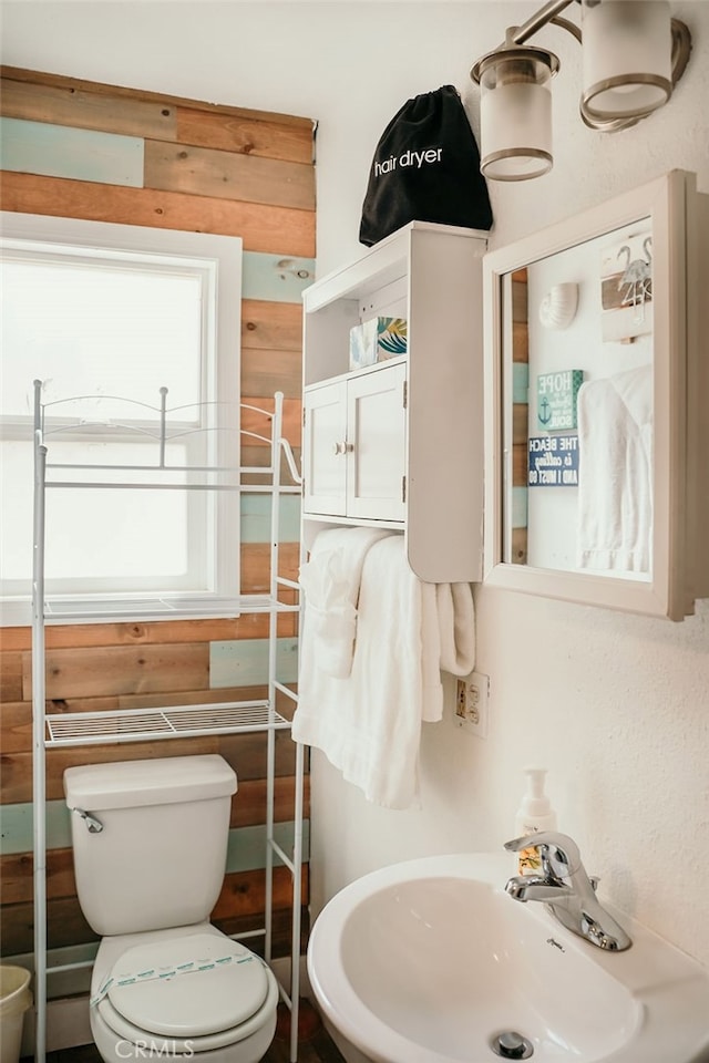 bathroom with toilet, wooden walls, and sink