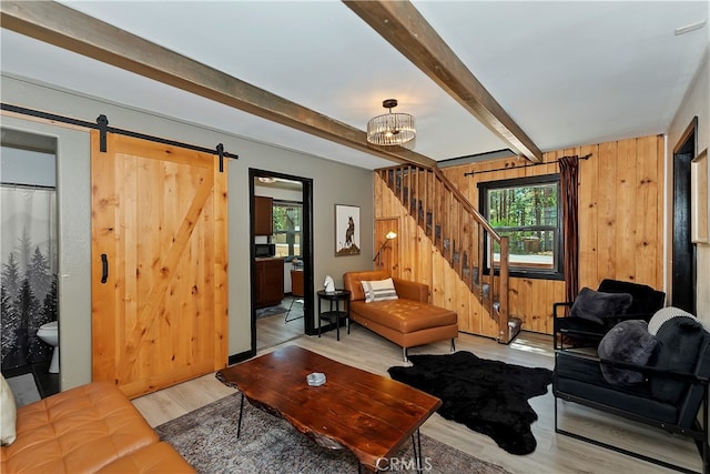 living room featuring light wood-type flooring, a chandelier, beamed ceiling, a barn door, and wooden walls