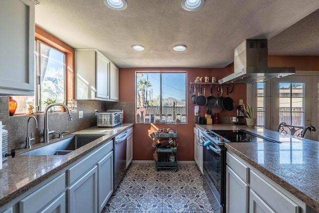 kitchen with white cabinets, island exhaust hood, appliances with stainless steel finishes, light stone countertops, and sink