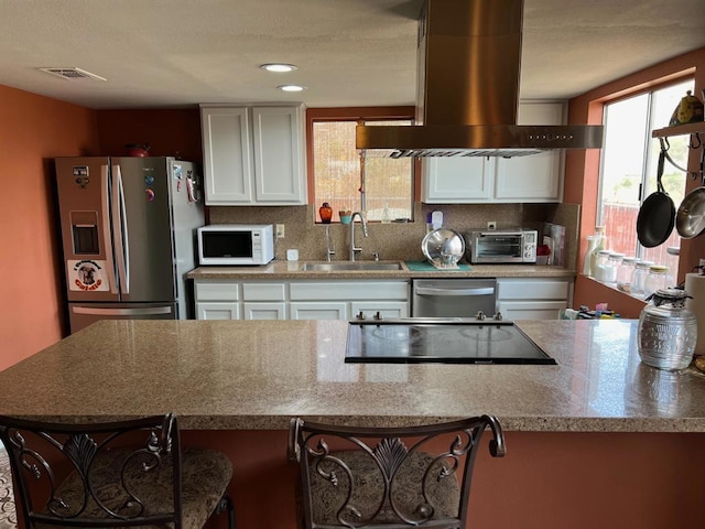 kitchen featuring stainless steel appliances, white cabinets, island range hood, and sink