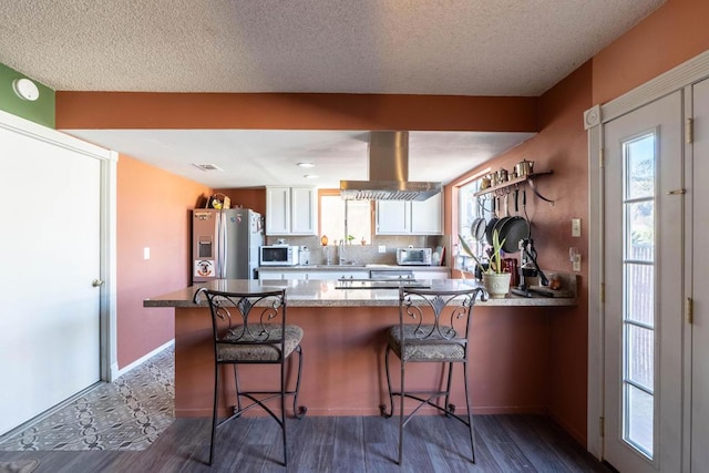 kitchen featuring kitchen peninsula, exhaust hood, stainless steel fridge, a breakfast bar area, and white cabinetry