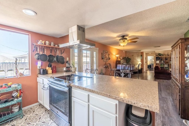 kitchen featuring island range hood, ceiling fan, stainless steel electric range oven, light stone counters, and white cabinetry