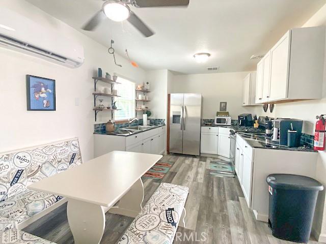 61974 Terrace Dr, Joshua Tree, CA 92252 - kitchen featuring appliances with stainless steel finishes, open shelves, a wall mounted air conditioner, ceiling fan, and light wood-type flooring