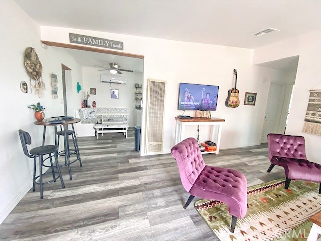 living room with a wall unit AC, hardwood / wood-style flooring, and ceiling fan