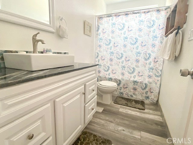 bathroom with a shower with shower curtain, hardwood / wood-style flooring, vanity, and toilet