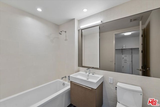 full bathroom with tile walls, tiled shower / bath combo, vanity, and toilet