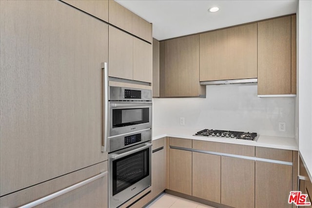 kitchen featuring light brown cabinetry, appliances with stainless steel finishes, light tile patterned floors, and extractor fan